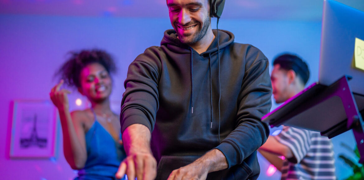 Group of diverse man and woman dancing with DJ mixing music on console. Attractive young teenager friends having fun with DJ mixing and scratching music mixer controller at house party with neon light